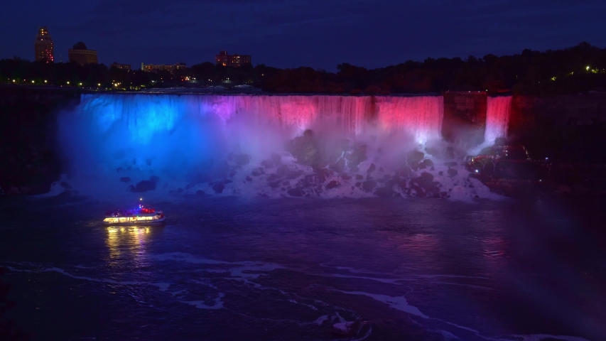 American Falls lit by colorful lights at night and a boat or cruise touring by, Niagara Falls, Ontario, Canada