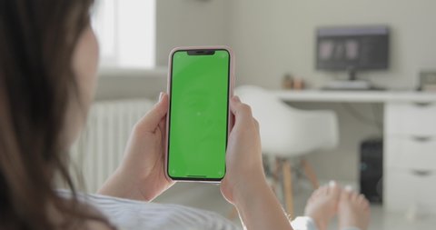 New York, USA - February 18, 2020: Woman use of smartphone with green screen, chroma key. iPhone X or XS Max, 11 Pro Max vertical orientation, modern apartment interior background. POV. 