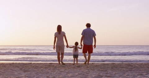 Happy family on the beach holding hands walking towards ocean at sunset on vacation slow motion RED DRAGON