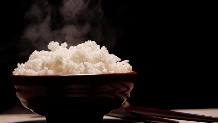 Hot cooked rice with steam in a bowl on black background in slow motion. Shot of hot steam rice Royalty-Free Stock Footage #1047262306
