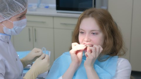 Orthodontist doctor putting silicone invisible transparent braces in girl's teeth in stomatology clinic. Portrait of teen girl. Correcting teeth. Oral hygiene and treatment, cure in dentistry.