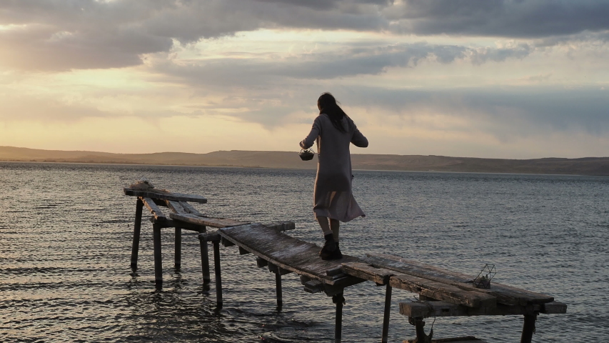 Teenager girl walking across vintage wooden bridge in an old tourist town, back view