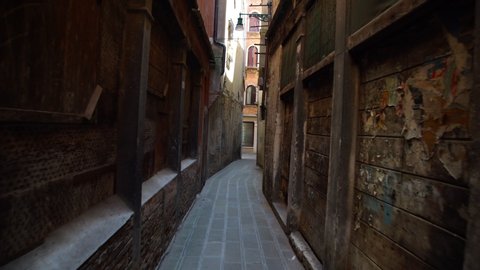 camera moves slowly along narrow historical shady street with old ragged brick houses and wooden doors in summer Venice
