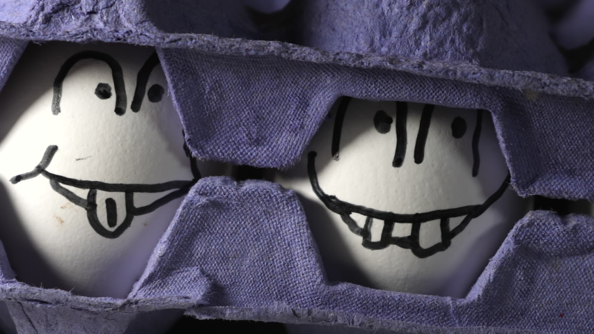 The white eggs with drawn faces in between two blue trays used for Easter egg hunting