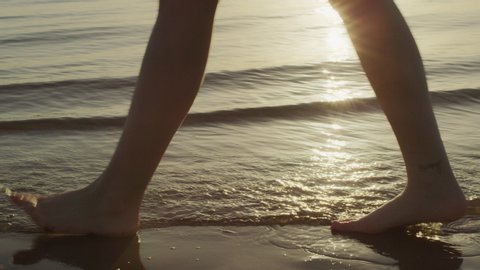 Woman's feet walking by on a beach in silhouette with lake in the background and sun glistening in the water in Australia. Close up on 4k RED camera.