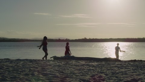 Friends playing cricket on the beach in silhouette with lake and sun in the background in Australia. Wide shot on 4k RED camera.
