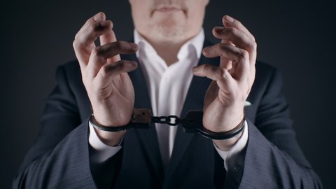 Close-up arrested man wearing formal suit shows his hands in handcuffs. Male businessman handcuffed for corruption crime with money laundering