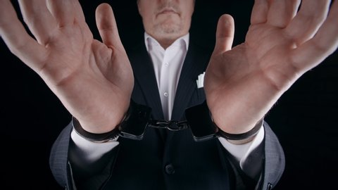 Arrested man wearing formal suit shows his hands in handcuffs. Male businessman handcuffed for corruption crime with money laundering. Close-up wide angle shot