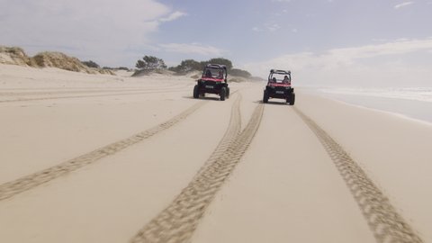 Two ATV vehicles racing on a beautiful beach with ocean and open sky in the background in Australia. Wide angle on 4k RED camera.