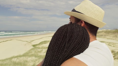 Couple standing at the edge of beach holding each other and saying goodbye, sand dunes in the background in Australia. Close up on 4k RED camera.