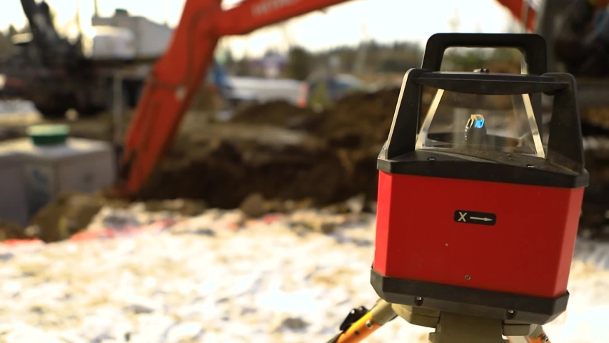 Close up selective focus footage of a spinning laser level at work during the installation of new septic tanks, a blurry excavator digs in background with copy space Royalty-Free Stock Footage #1047304000
