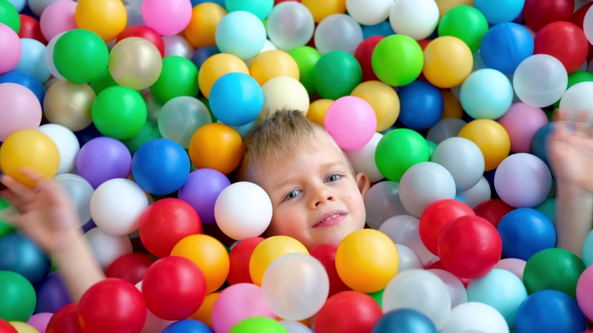 Blonde little boy lying on multi coloured plastic balls in big dry paddling pool in playing centre. Smiling at camera. Portrait close up. Having fun in playroom. Leisure Activity. | Shutterstock HD Video #1047306928