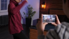 Close-up of curly mixed race teenager stylishly dancing while his caucasian friend holding smartphone and taking video. Diverse teenage friends having fun while shooting video during domestic leisure