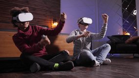 Joyful mixed race friends in VR glasses spending domestic leisure driving cars in virtual reality. Modern diverse teenagers in augmented-reality goggles enjoying joint racing in cyberspace