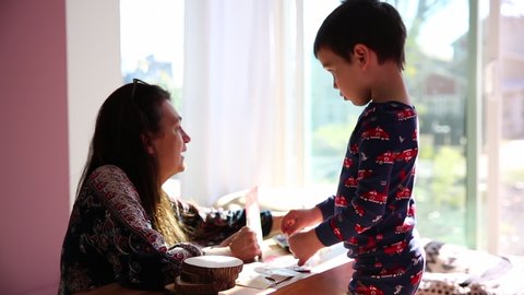 Grandmother talking to toddler boy as he makes arts and crafts in living room early in the morning