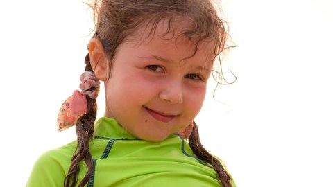 From below of adorable little girl with wet hair and face dressed in bright green shirt looking at camera and smile against clear sky