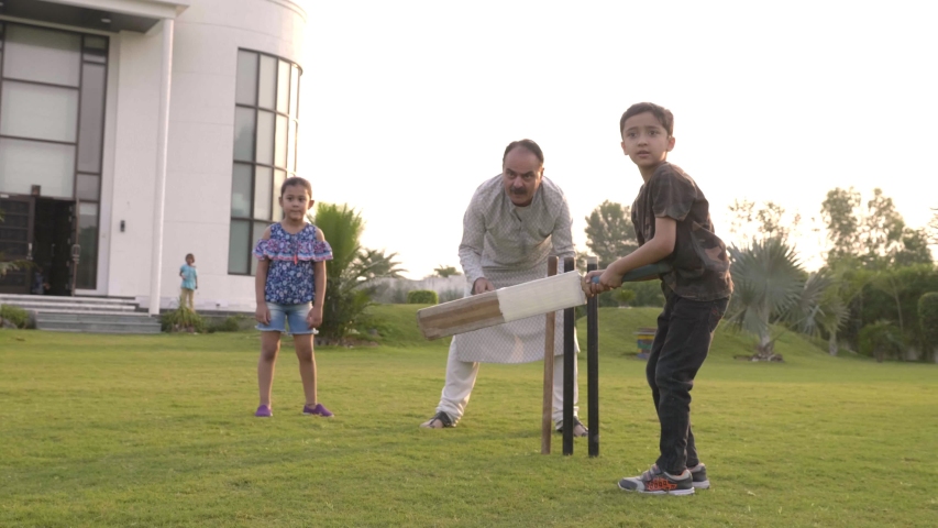 A young active boy batting hits the ball with the bat and celebrates outdoors. A male kid strikes the ball for four runs while playing cricket with his family members in the garden outside the house  Royalty-Free Stock Footage #1047311134