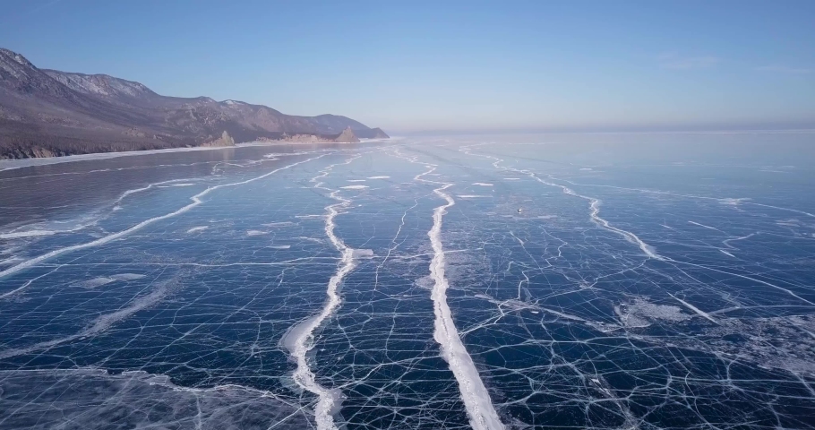 Frozen lake. Deep blue ice, hummocks, cracks Beautiful winter landscape with transparent smooth ice.