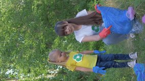 ecological care, little child girl helps mom to collect plastic and polyethylene litter in garbage bag while cleaning nature near pointer sign in green grass outdoors, orientation 9:16