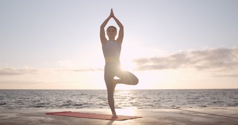 Doing yoga at sunrise, the girl practices the yoga tree pose, the harmony of the body with nature. Stock Video