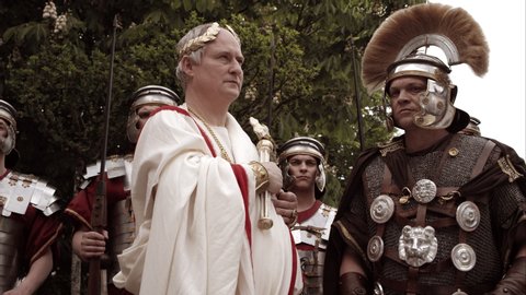 Emperor Holds Out Scepter And Says Something While Centurion Stands Beside Him