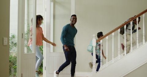 Side view of an African American couple with young son and daughter entering the front door in their new home, the children running up the stairs wearing backpacks, slow motion 