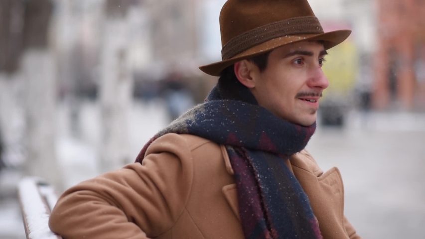 The guy is drinking hot tea on the street. A man enjoys coffee on a bench in winter.