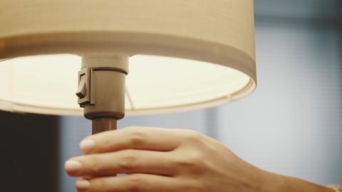 Woman turning on a table lamp at home, hand close up