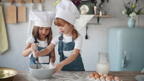 Two kids in white chef uniform mixing flour in bowl on the kitchen.