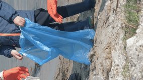 plastic pollution, man and woman with kid boy in rubber gloves collects trash in garbage bag while cleaning dirty beach close up, orientation 9:16