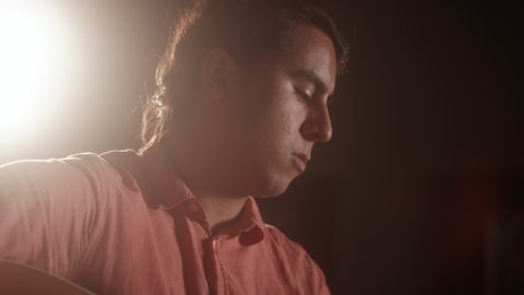 A young male musician of latino descent playing acoustic guitar on stage with a lens flare