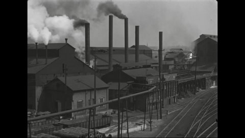 CIRCA 1930s - Train cars travel near a factory which is producing large amounts of smoke.