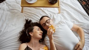 Young couple lying on bed, they are eating croissant, happy together. Morning breakfast in bed, romantic scene. Smiling, having fun, funny family. Two travelers in hotel. - Powered by Shutterstock - Get 15% off with code: PIKWIZARD15