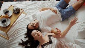 Young couple lying on bed, they are happy together. Morning breakfast in bed, romantic scene. They hold hands, smile, with closed eyes. Two travelers in hotel, travel together. - Powered by Shutterstock - Get 15% off with code: PIKWIZARD15