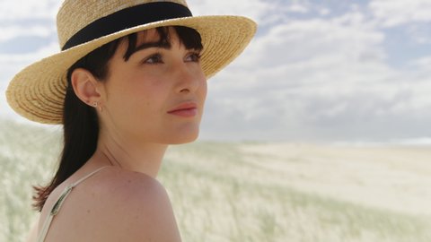 Beautiful brunette woman wearing a hat looking out at the ocean on a beach in Australia with soft natural lighting. Close up shot on 4k RED camera.
