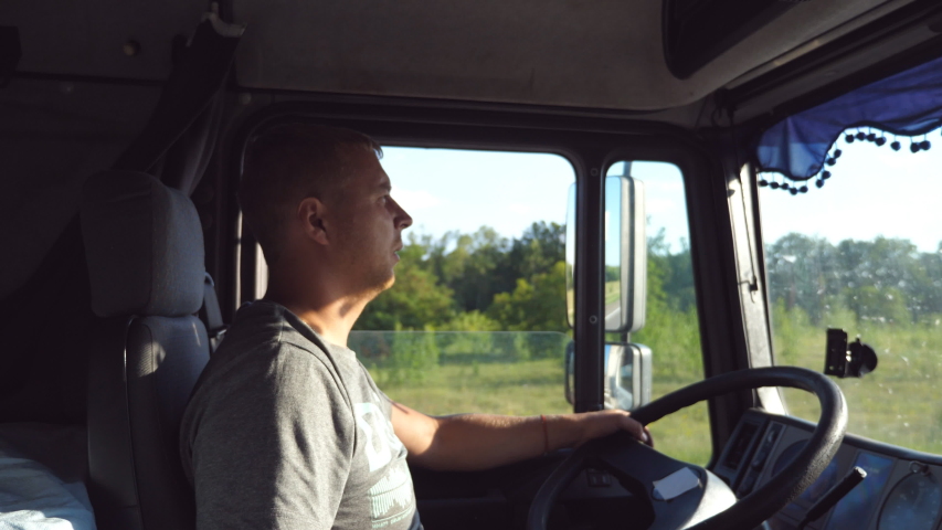 Man holds hand on the steering wheel and driving truck through countryside. Truck driver profile. Trucker sitting at the wheel of the car. Caucasian guy looks carefully at the road. Side view Close up Royalty-Free Stock Footage #1047359836