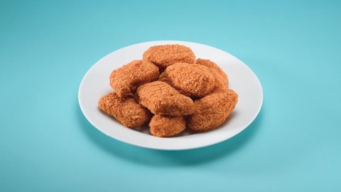 A stop motion video of delicious chicken nuggets being eaten, one by one until only crumbs are left on a white plate, on top of a blue background. Teal and orange colors.