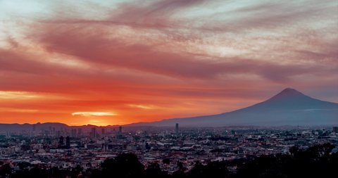Puebla de Zaragoza overview at orange sunset with beautiful moving clouds and Popocatepetl volcano in background, motion time lapse clean city for reduction of pollution because of Covid-19.