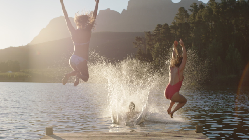 Happy friends running jumping off jetty in lake at sunset having fun splashing in water enjoying freedom sharing summertime adventure | Shutterstock HD Video #1047368257