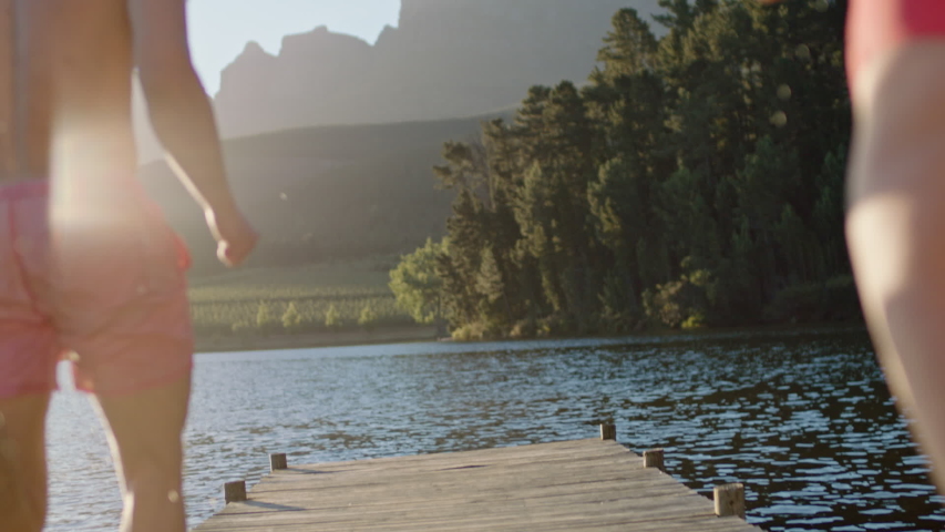 teenage friends running jumping off jetty in lake at sunset having fun splashing in water enjoying freedom sharing summer adventure on vacation