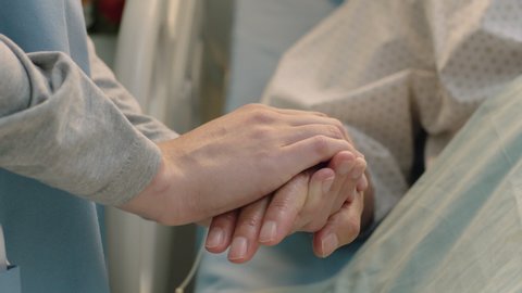 hospital nurse holding hand of old woman in bed comforting elderly patient hospitalized recovering from illness medical professional at bedside giving encouragement health care support