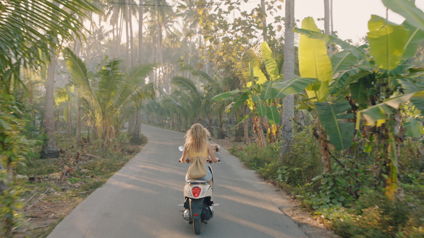 travel woman riding motorcycle on tropical island enjoying road trip adventure on motorbike scooter rear view