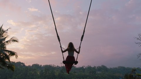 tourist woman swinging over tropical jungle at sunrise travel girl enjoying exotic vacation sitting on swing in having fun holiday lifestyle freedom 4k - Βίντεο στοκ
