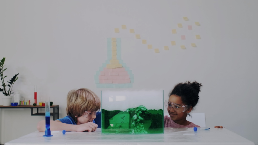 Chemical Experiment in Science. Cheerful Diverse Pupils in Classroom or Lab. Blond Boy and Curly African American Cute Girl puts dry Ice in Glass container with Liquid Nitrogen. Royalty-Free Stock Footage #1047374389