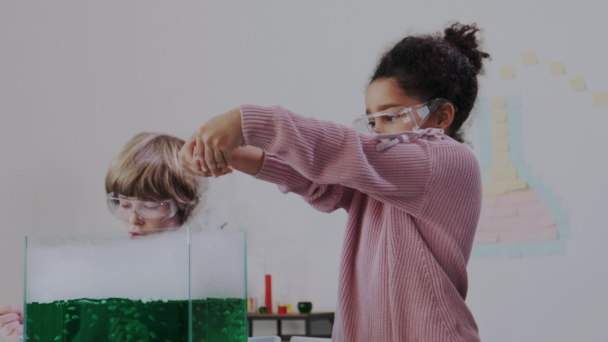 Closeup. Playing with Smoke and Steam in Chemical Lab or Classroom. Clever Blond Boy and Dark-skinned Little Girl Explore Chemical Reactions in Liquid. Education, Modern Knowledge, Practice. Royalty-Free Stock Footage #1047379783