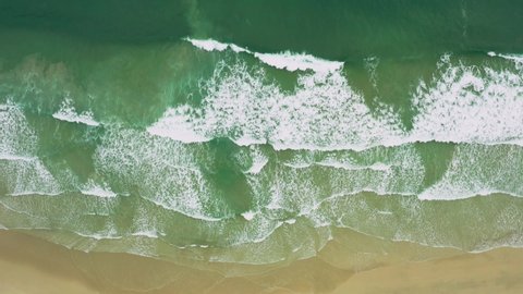 Aerial views of flying over stunning sandy beach with tropical waves rolling into the shore.