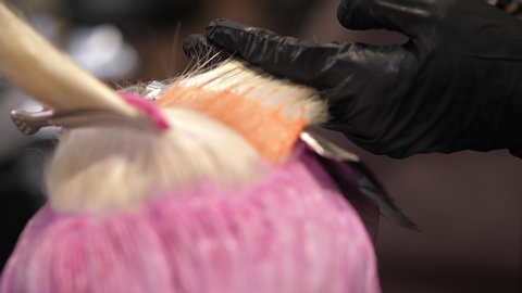 Close-up of stylist hands using professional hairbrush and dyeing hair roots of young female client. Stylish and high-quality pink tint in beauty salon, the process of applying color on hair. 4
