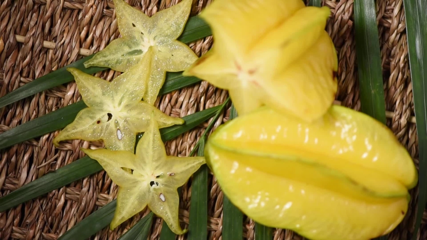 Yellow carambola fruit on rotating background. Top view. Exotic fruits, tropical palm branch. Vegan and raw food concept.