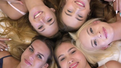 home party, pretty and funny girls with beautiful makeup in pajamas at bachelorette party waving into camera while lying on bed into room, orientation 9:16