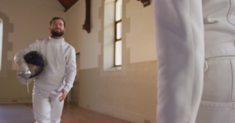 Front view of a Caucasian and a mixed race male fencer athletes during a fencing training in a gym, holding masks, smiling, shaking hands after finished fencing duel, in slow motion